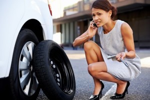 Woman calling for assistance with flat tire on car in the city